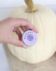 A close-up of a hand holding a tin of Lavender purple pocket sized tin of SOOTHE Everything salve.
