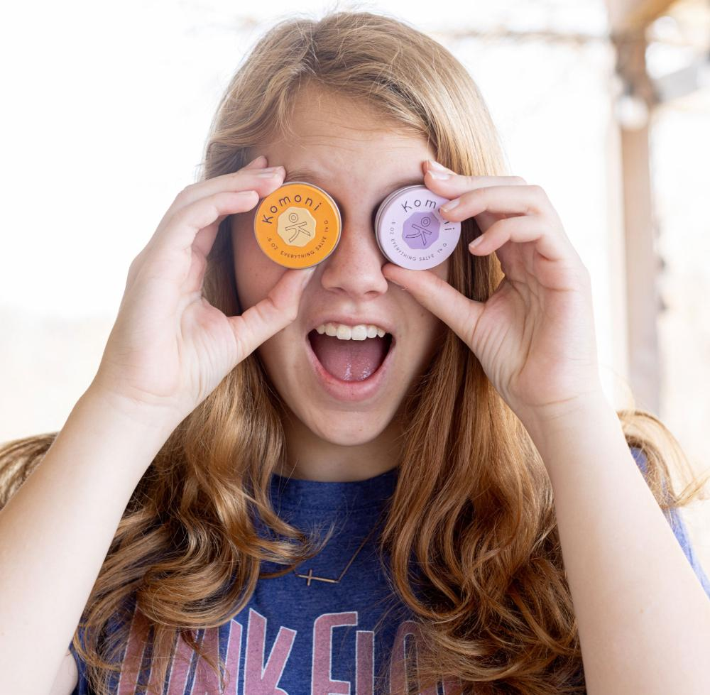 Image of a young woman playfully holding a pair of Everything Salve tins up to her eyes like binoculars.