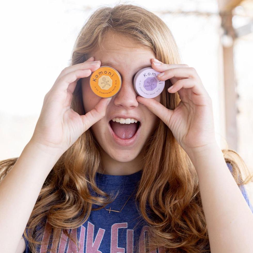 Image of a young woman playfully holding a pair of Everything Salve tins up to her eyes like binoculars.