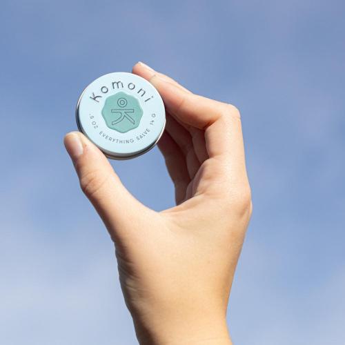 Breath pocket-sized Everything Salve held up to the sky fits comfortably in the palm of your hand.