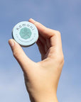 Breath pocket-sized Everything Salve held up to the sky fits comfortably in the palm of your hand.