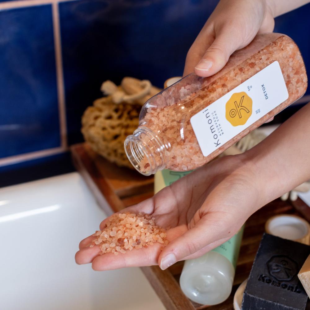 Detox Bath Soak shown being dispensed into a bath. Crafted with ethically sourced Himalayan Salt and enriched with a soothing blend of essential oils, this soak will leave your skin smooth and refreshed with the invigorating yet calming aroma blends of Lavender, Peppermint, Grapefruit, and Patchouli essential oils.