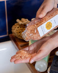 Detox Bath Soak shown being dispensed into a bath. Crafted with ethically sourced Himalayan Salt and enriched with a soothing blend of essential oils, this soak will leave your skin smooth and refreshed with the invigorating yet calming aroma blends of Lavender, Peppermint, Grapefruit, and Patchouli essential oils.