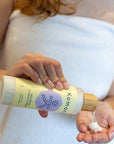 A woman in a bath towel dispensing all-natural nourish shampoo or conditioner with essential oils into her hand from an 8 oz. bottle with elegant bamboo top.