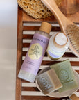 Nourish Lavender Shampoo and Conditioner shown with a Shampoo Bar and Face & Body Cleanser Bar with other items like a sponge and bath brush. 