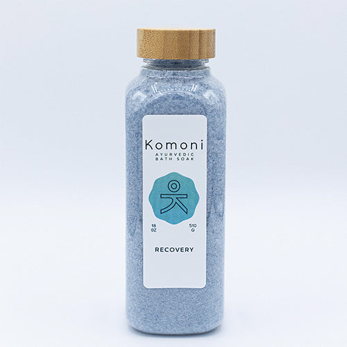 Light indigo crystals of RECOVERY Bath Soak in 18 oz. clear plastic bottle with bamboo wood top.