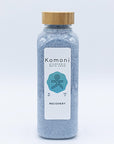 Light indigo crystals of RECOVERY Bath Soak in 18 oz. clear plastic bottle with bamboo wood top.