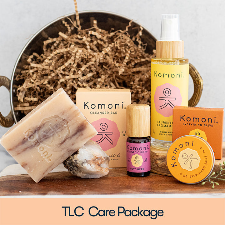 The TLC Care Package features grapefruit-geranium essential oil cleanser bar, 10 mL bottle of love herb ayurvedic pure essential oil blend, Laurentha essential oil aromamist, and uplift patchouli essential oil everything salve.