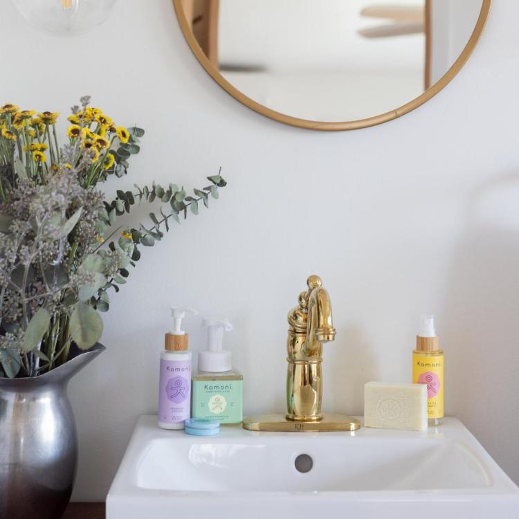 Nourish body lotion, Breathe Everything salve, Rosemary-Mint Everything Soap, Face and Body Cleanser Bar, and Laurentha Aromamist shown together on a white porcelain sink. 