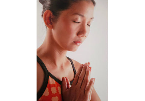 Komoni founder demonstrating fitness connection in a meditative yoga-like pose with hands together in prayer. 