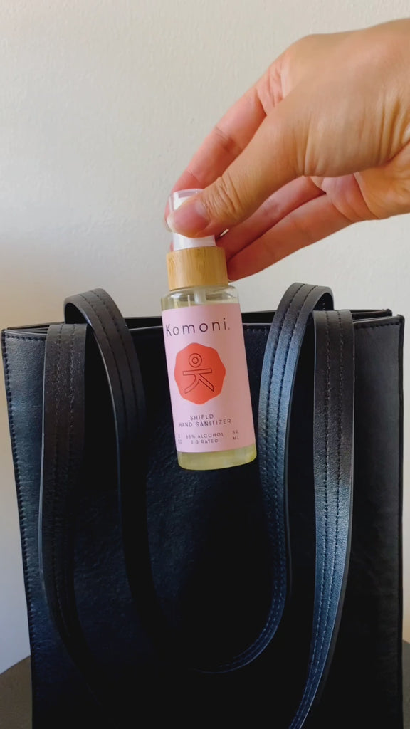 Palm-sized 2 oz. spray bottle of Komoni moisturizing hand sanitizer being placed into a leather handbag.