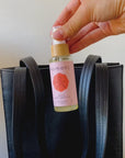 Palm-sized 2 oz. spray bottle of Komoni moisturizing hand sanitizer being placed into a leather handbag.