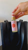 Palm-sized 2 oz. spray bottle of Komoni moisturizing hand sanitizer being placed into a leather handbag.