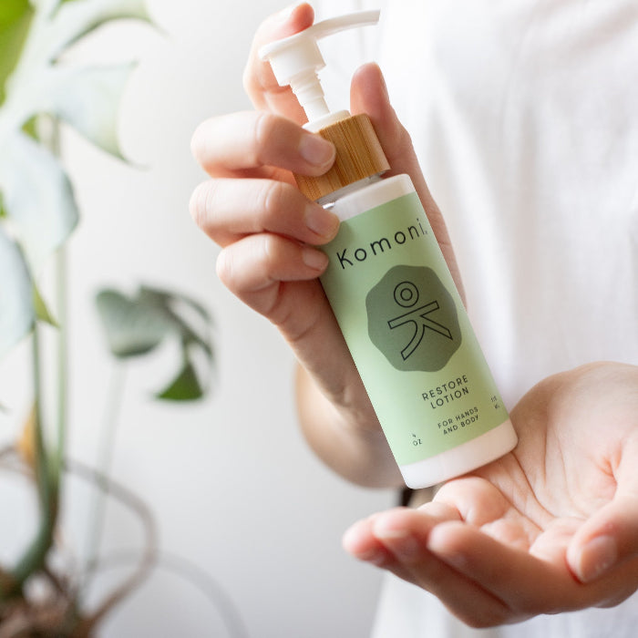 Hands holding a wood top 4 oz. pastel green pump-bottle of RESTORE pure botanicals lotion.