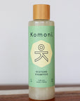 Wood top 8 oz. pastel-green bottle of Restore Botanical Shampoo with rosemary and other essential oils for all hair types.