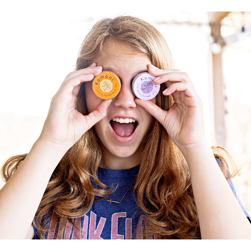 Image of a young woman playfully holding a pair of Everything Salve tins up to her eyes like binoculars.